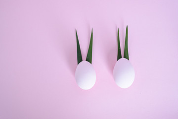 Two eggs with ears of leaves on a pink background.One leaf bent. top view. concept of minimalism eggs