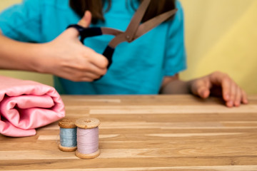 Set of tailoring accessories. Close up of a stack of folded pink fabric, sewing scissors, and spools of thread