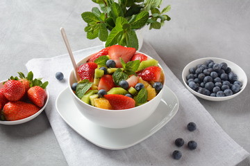 Bowl of healthy fresh colorful fruit salad on wooden background. Top view.Fruit salad with strawberry, blueberry, sweet cherry, kiwi.Vegetarian food concept. Rustic wooden background