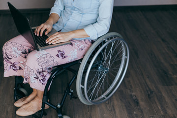 Woman in a wheelchair at home with a laptop on her lap, hand close up, unrecognizable man.