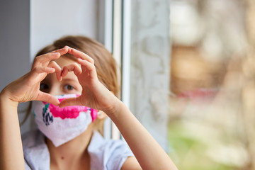 Little girl, child in mask making hearts from hands, coronavirus quarantine