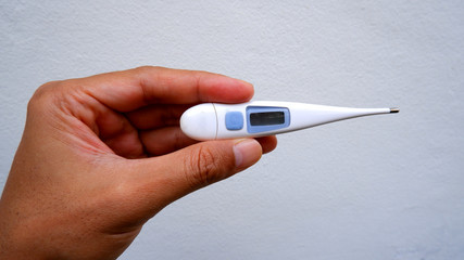 Hand holding thermometer on white concrete background