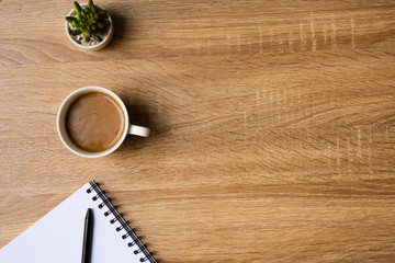 desk office with blank notepad, coffee cup and pen on wood table. Flat lay top view copy spce.
