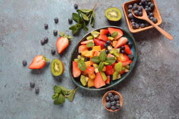 Bowl of healthy fresh colorful fruit salad on wooden background. Top view.Fruit salad with strawberry, blueberry, sweet cherry, kiwi.Vegetarian food concept. Rustic wooden background