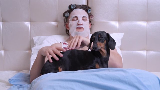 man neatly and gently strokes the dog with his dog dachshund in the bed.