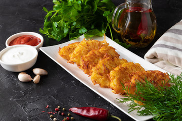 Potato pancakes with sauces and fresh herbs on a dark background. Ukrainian and Belorussian national cuisine