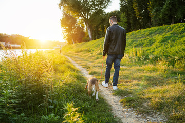 Young man takes his beloved dog for a walk in the park at sunset - Millennial in a moment of...