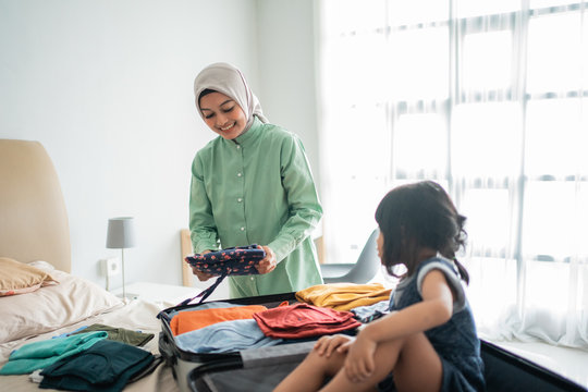Asian mother prepares clothes to be taken away to put in a suitcase when accompanied by her daughter is playing