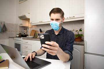 Fototapeta na wymiar Working from home during Coronavirus outbreak. Business man working from home wearing protective mask. Portrait of man sitting at his desk in the small apartment kitchen