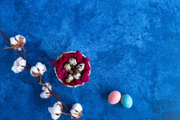 Obraz na płótnie Canvas Decorative quail easter eggs in red nest on dark blue background. Holiday decorations, Easter concept background.
