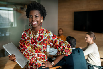 Beautiful young smiling professional black african business woman holding laptop, coworkers hold a...