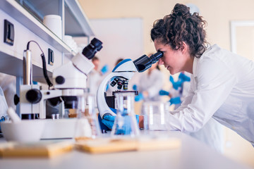 Young female scientist looking through a microscope in a laboratory doing research on finding...
