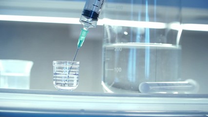 Close up of syringe in laboratory takes medical solution from beaker for chemical analysis. Сoncept of pharmaceutical research. Concept of Coronovirus Vaccine Development. - Powered by Adobe