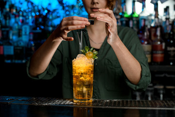 Young woman bartender carefully decorate by powder glass with cocktail.