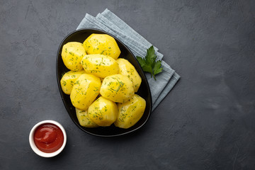 Delicious boiled potatoes with dill and ketchup on a black background. Top view, flat lay.