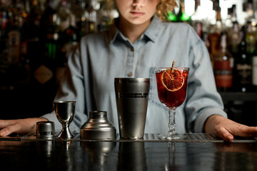Tools for making cocktail and glass of drink stand on bar counter.