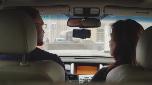 Woman on passenger seat points the direction with her finger then looks on the right and smiles, tlking happily to male driver. Back view.