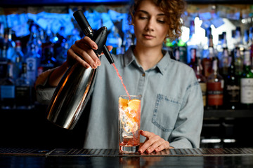 young bartender woman energetically pouring cocktail using steel siphon