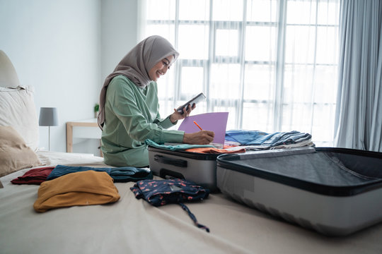 hijab woman sitting on the bed while looking at the list of items to be taken away on vacation