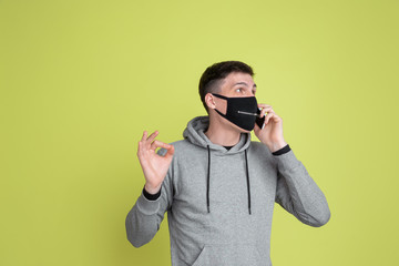 Talking on phone. Caucasian man's portrait isolated on yellow studio background. Freaky male model in black face mask. Concept of human emotions, facial expression, sales, ad. Unusual appearance.