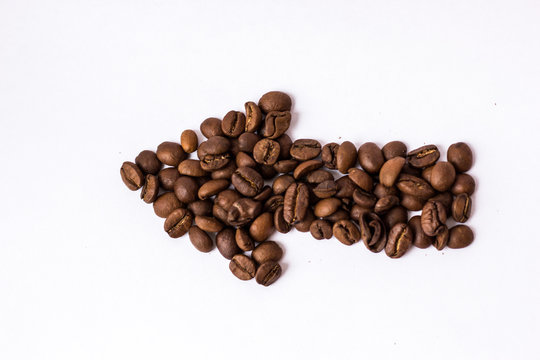 Roasted scattered coffee beans on white background in the shape of an arrow