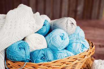 Fototapeta na wymiar Women's hobby. Crochet and knitting. Working space. Blue yarn in basket, flowers, knitting needles, scissors, crochet hooks on the wooden background in the cozy home in rustik style.