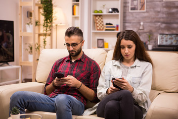 Boyfriend and girlfriend using their phones while sitting together on couch