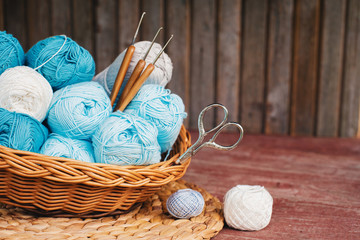 Women's hobby. Crochet and knitting. Working space. Blue yarn in basket,  knitting needles, scissors, crochet hooks on the wooden background in the cozy home in rustik style.
