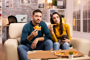 Gorgeous young couple eating pizza while watching TV