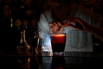 close-up of glass with red cocktail on which female bartender sprinkles by citrus.