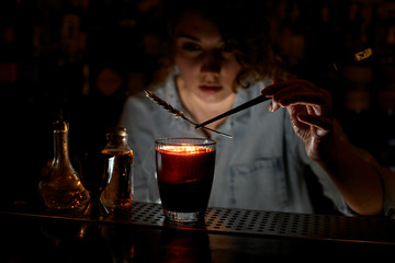 Woman barman carefully decorates red cocktail with spikelet using tweezers