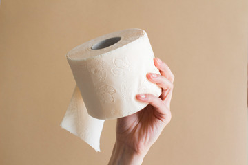 woman's hand with a roll of peach beige toilet paper on beige background