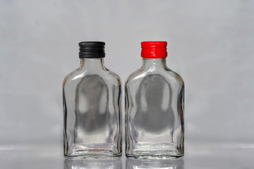 Two empty  russian vodka glass bottles with black and red caps on a grey background horisontal image
