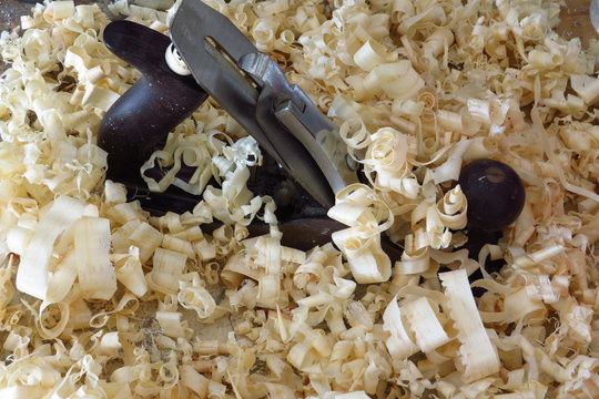 An old fashioned wood plane lies amongst the wood shavings it created.