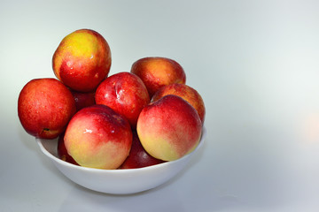 Few ripe red fresh nectarines peaches in a white bowl on a light background 
