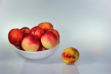 Few ripe red fresh nectarines peaches in a white bowl on a light background 