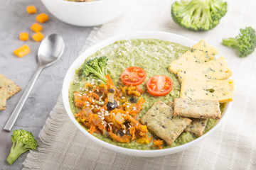 Green broccoli cream soup with crackers in white bowl on a gray concrete background, side view, selective focus.