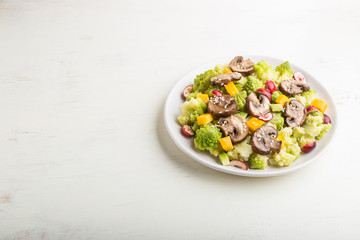 Vegetarian salad from romanesco cabbage, champignons, cranberry, avocado and pumpkin on a white wooden background. side view, copy space.