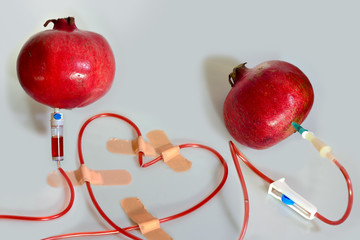 Two pomegranates connected by a medical dropper iv cannula with a pomegranate juice, shaped in a heart form, fixed by patches