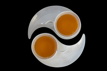 Two white cups with black tea are standing on two white plates against black background, top view