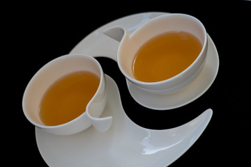 Two white cups with black tea are standing on two white plates against black background, closeup side view