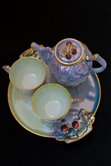 Closeup view of colorful ceramic vintage tea set standing on a tray on black background
