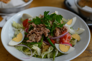 Fresh salad with tuna, eggs, lettuce, red onions and herbs in a deep white plate. Vegetarian option. A healthy, green and vitamin-rich dish. You can order in a cafe or an easy option for home cooking.
