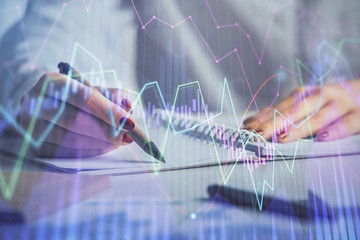 Double exposure of woman's hands making notes with forex graph hologram. Concept stock market analysis.