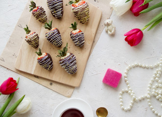 Flatlay in light colors: coffee, chocolate-covered strawberries, flowers.