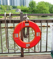 Bright orange lifesaver tied to a railing next to a river park