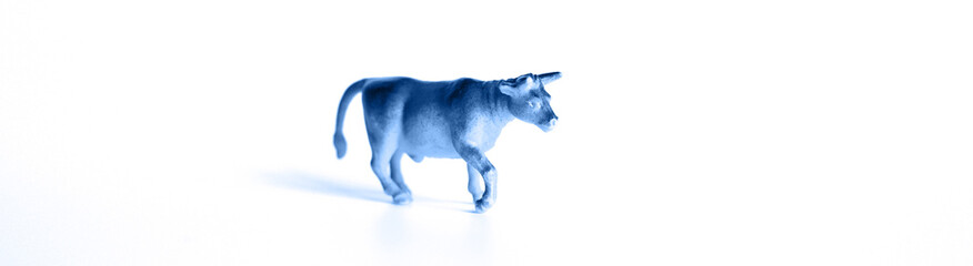 a small plastic toy figure of a bull is isolated on a white background. symbol of the year 2021 ox. banner. toned in classic blue color trend 2020 year