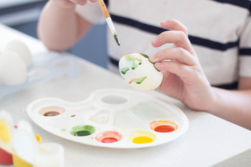 a child paints eggs with watercolors and gouache waits for Easter and plays