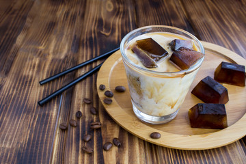 Cold milk  with coffee ice in the glass on the brown  wooden  background. Closeup.