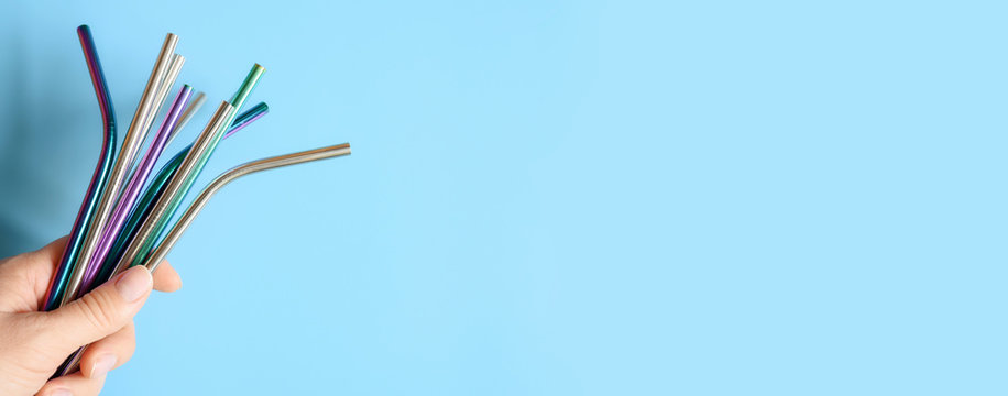several reusable metal stainless steel drinking straws in female hand on a blue background. space for text. banner